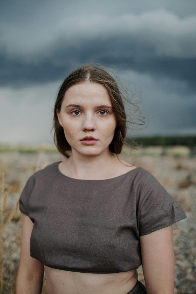 A woman stands outdoors with a dramatic, stormy sky in the background.