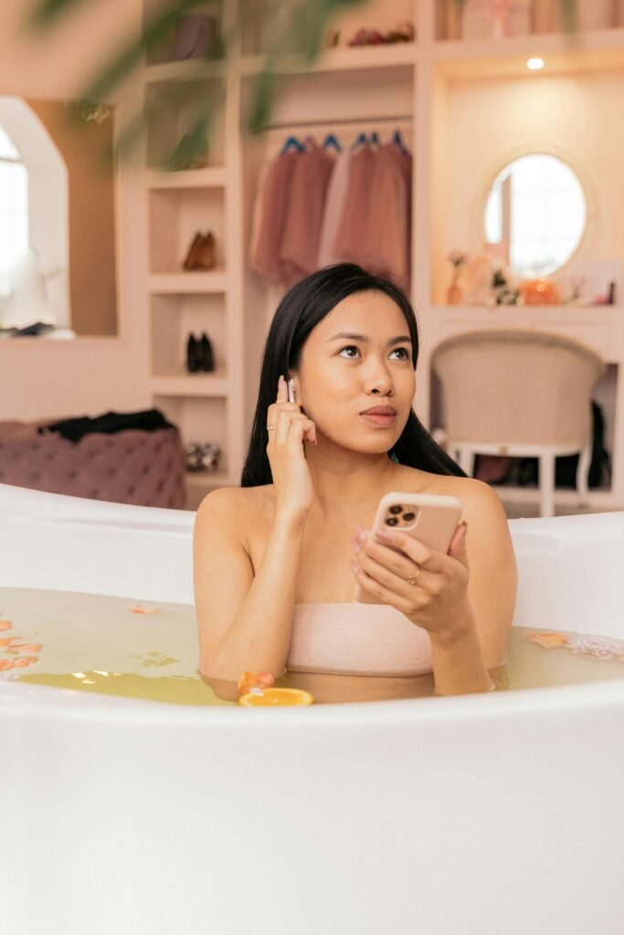 pexels-photo-6728326-6728326 Woman enjoying a calming bath with petals and using a smartphone for relaxation.